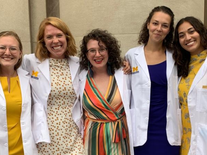 Group of five women wearing white medical coats and smiling