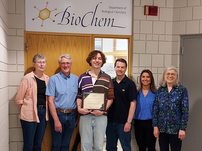 Ash de Borchgrave holding award certificate and flanked by advisors