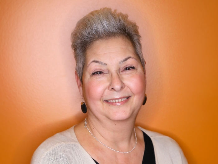 woman smiling with white short hair and earrings dark with orange background