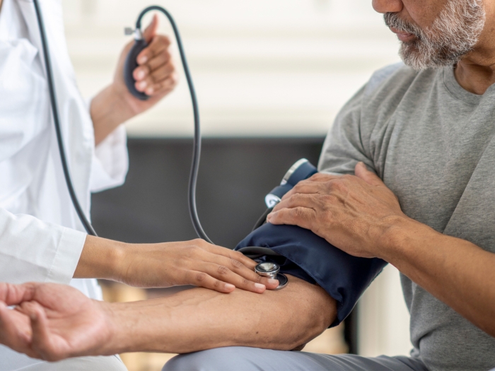 blood pressure cuff on mans arm with white coat doctor taking it 