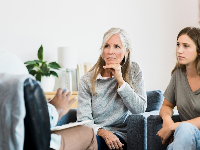 two women, one older one younger, looking concerned listening to a provider across from them with back to camera