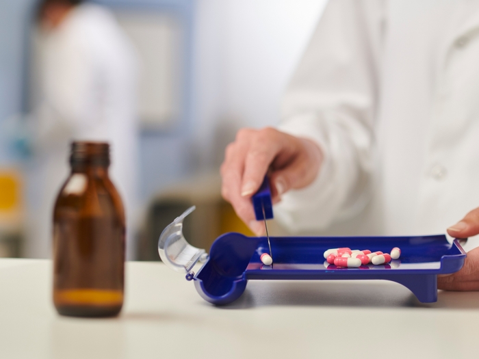 person at counter with medicine brown bottle and pills