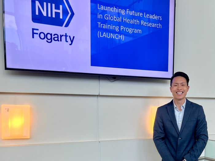 Man in a blazer standing next to a screen with a slide that reads 'NIH Fogarty'