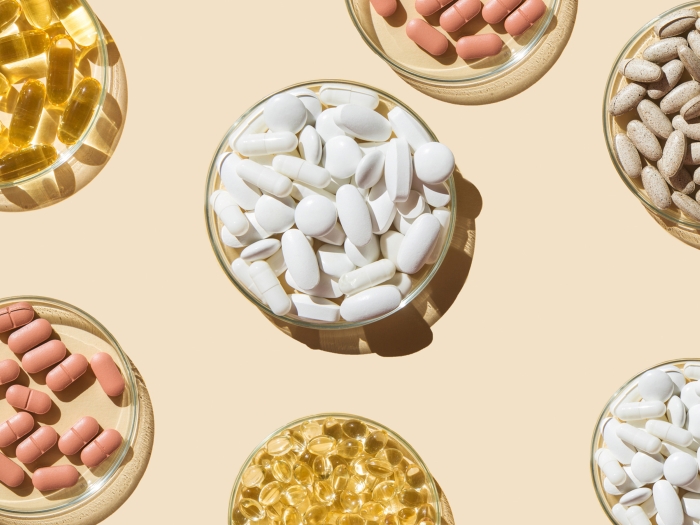 different color pills yellow pink white tan in small glass bowls on peach background