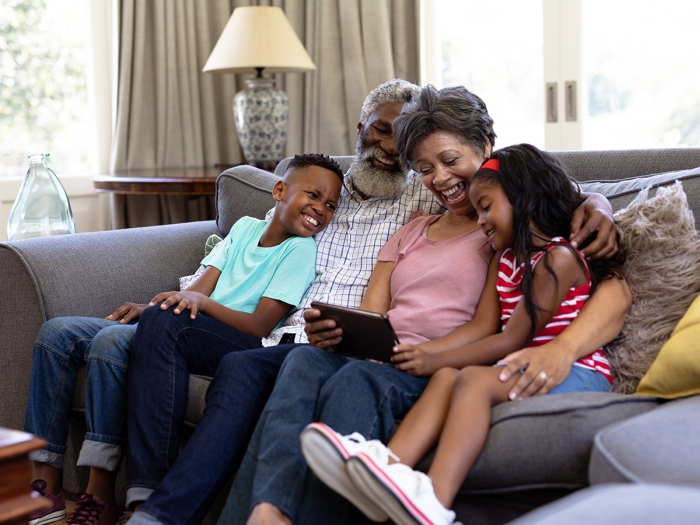 family of four sitting on couch in living room looking at an ipad laughing