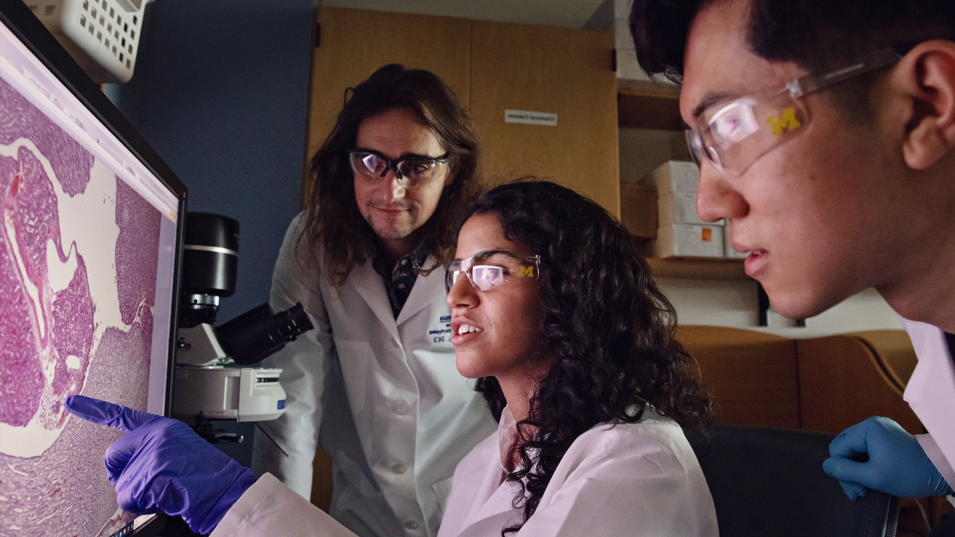 Three people looking at a computer screen with lab goggles