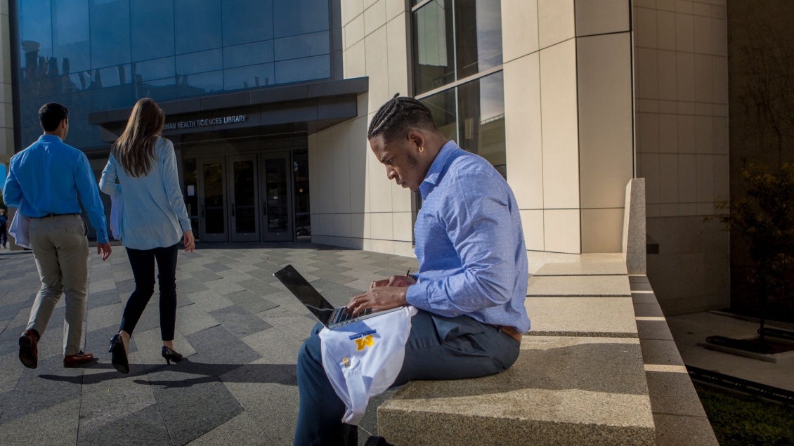 Person sitting outside a building working on a laptop