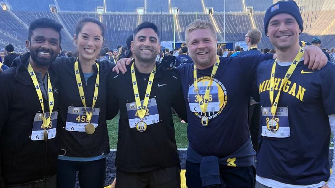 Group of men standing at the Big House wearing maize and blue, medals and name badges