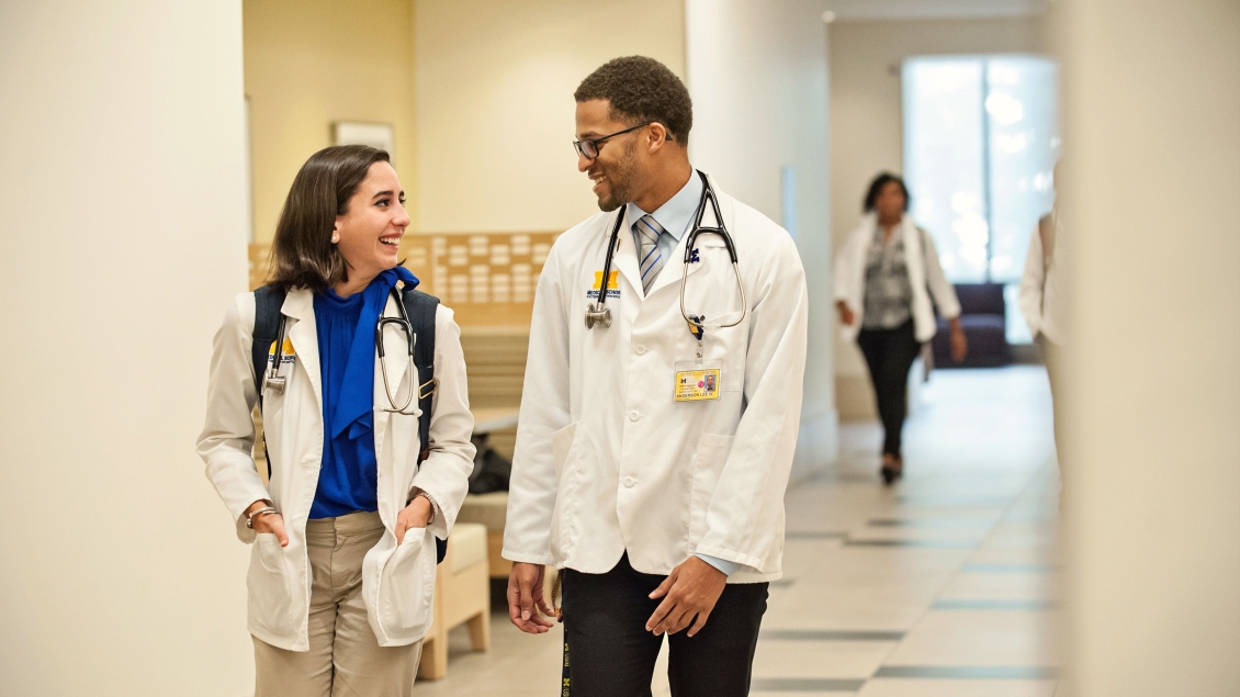 Two people in lab coats walking down a hallway