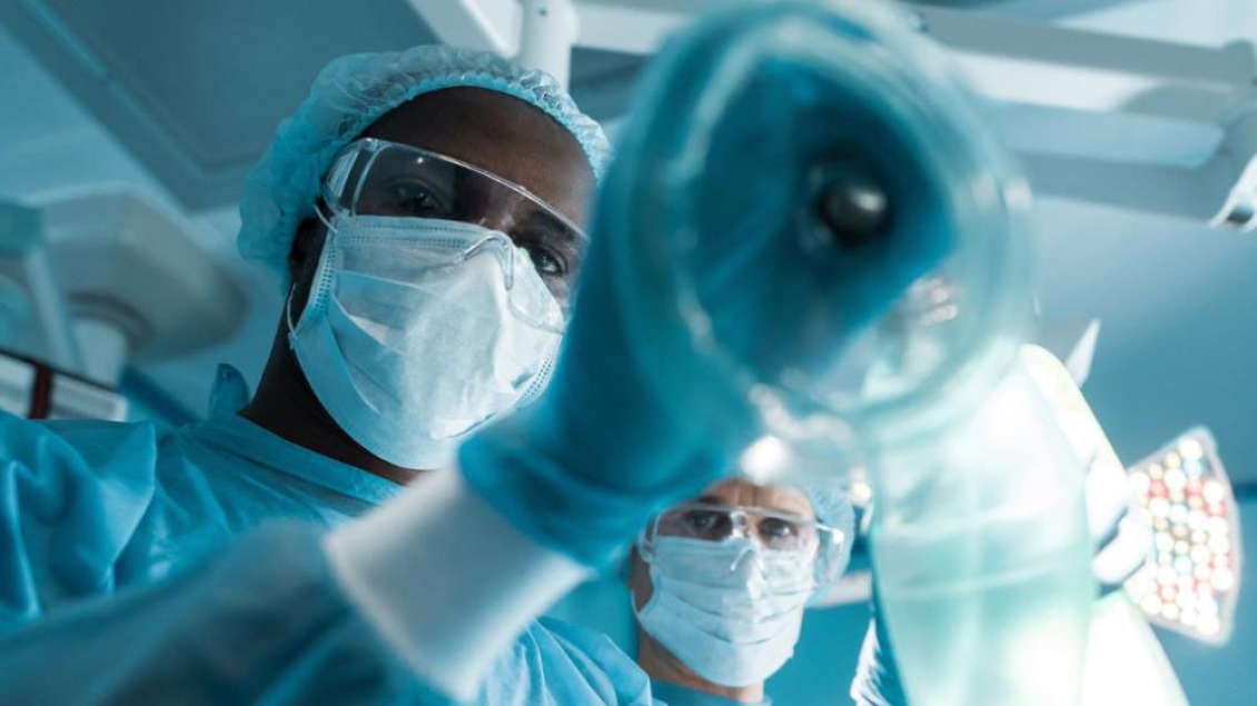 An anesthesiologist in surgical scrubs holds a face mask.