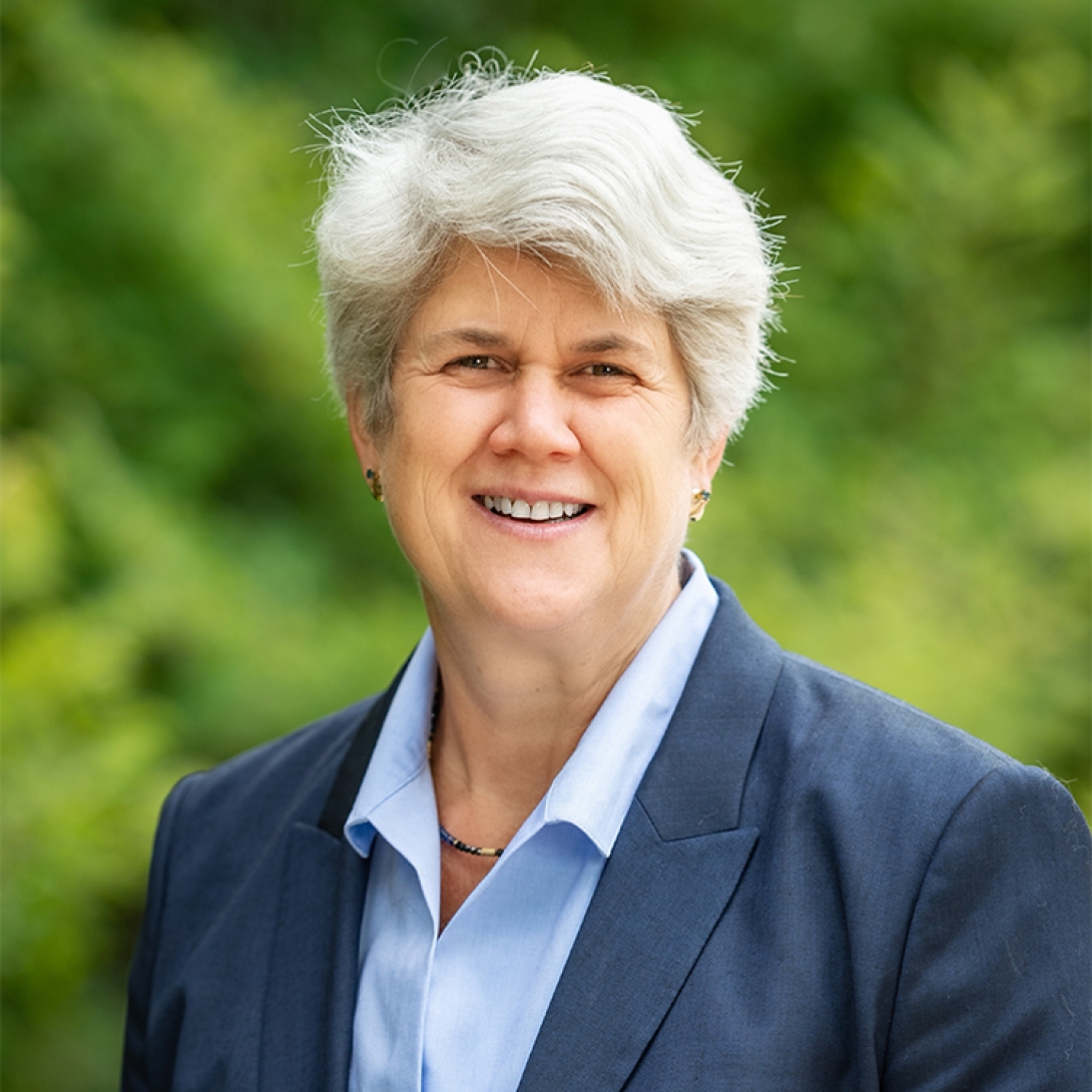 Headshot of Quinta Vreede wearing light blue shirt and blue jacket with trees in background