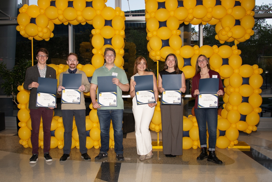 Group photo in front of a balloon backdrop, holding certificates